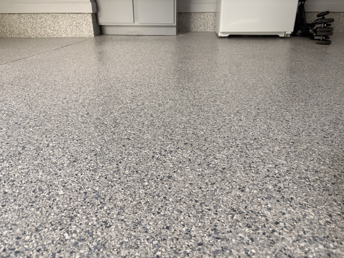 Floor-level view of the cured flake floor in Tipton, showing the gloss of the polyaspartic topcoat and the flake cove base running up the wall.